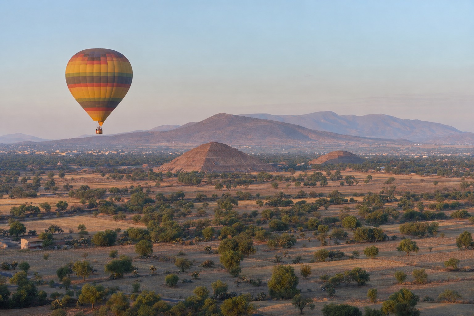 A hot air balloon over the Teotihuacan valley at sunrise with the pyramids in the distance