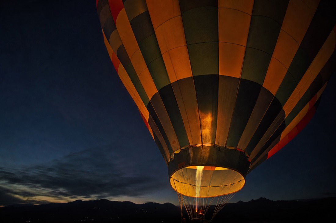 A single hot air balloon catching early light against a still-dark sky