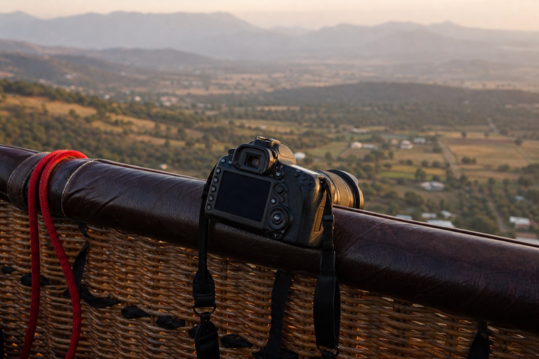 A camera on a neck strap resting against a hot air balloon basket rim