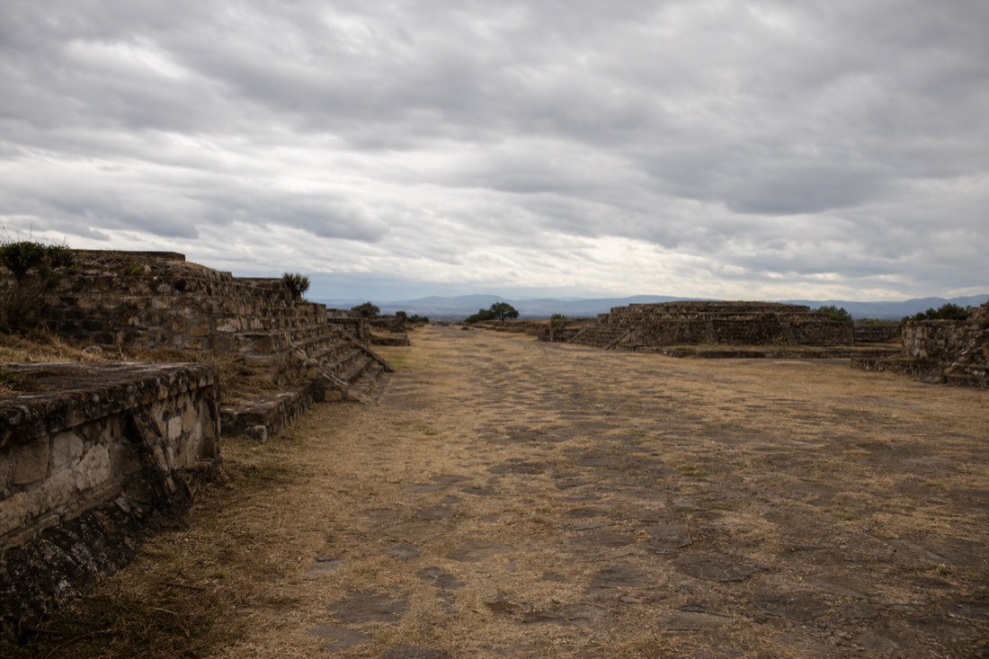 Ruined stone platforms along an ancient avenue under an overcast sky