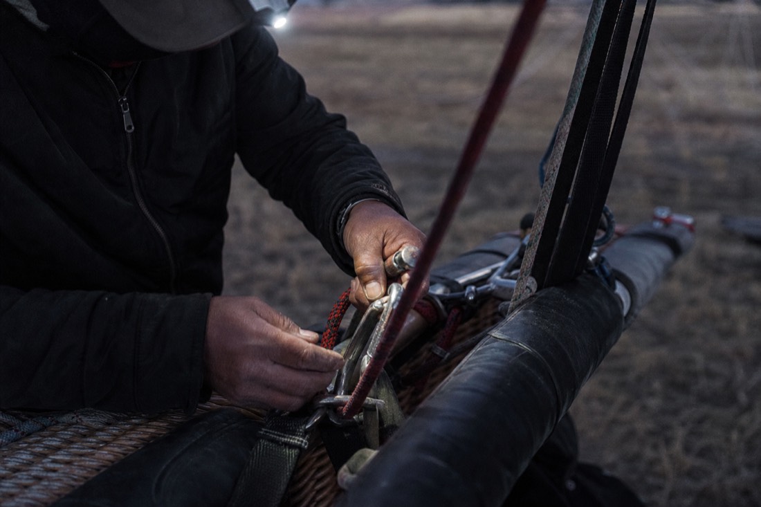 A ground crew member checking rigging on a hot air balloon basket before dawn
