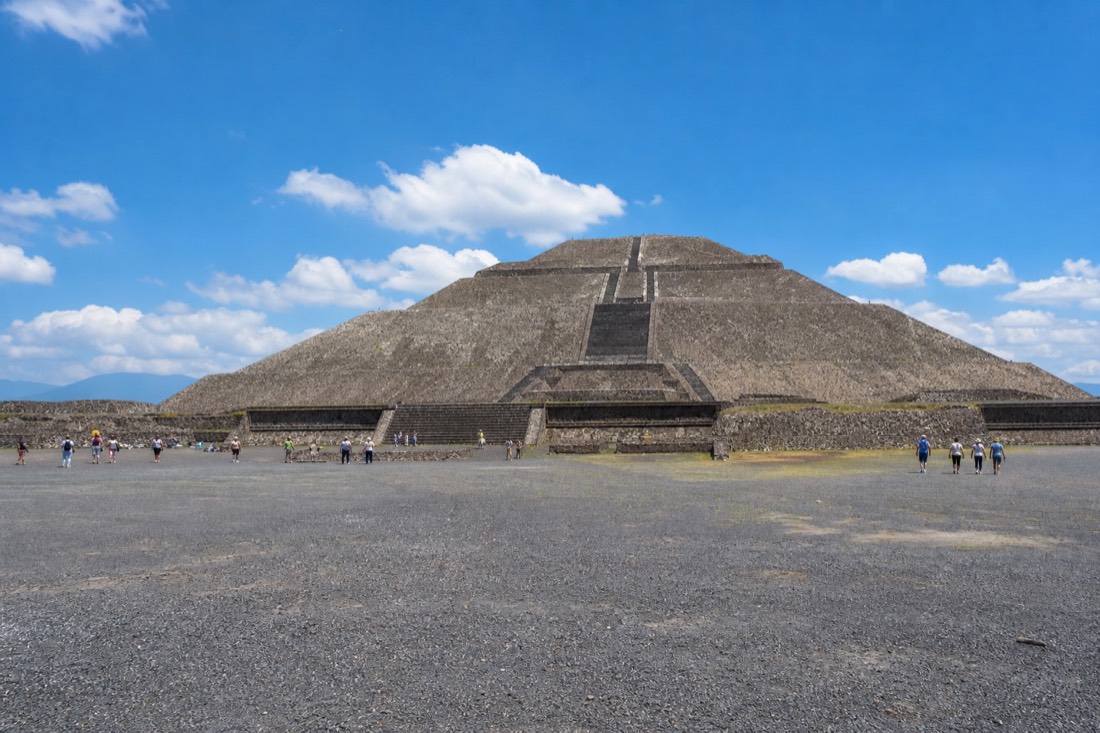 A wide stone plaza at the base of a large stepped pyramid at midday