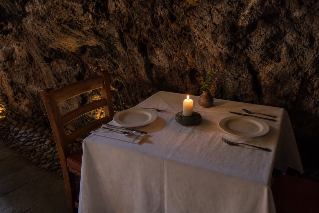 A rustic table set with a white cloth and candle against a volcanic cave wall