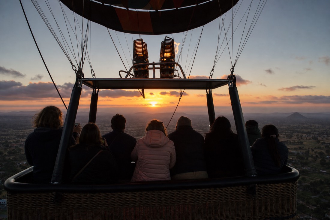 A group of friends at the rail of a shared hot air balloon basket at sunrise