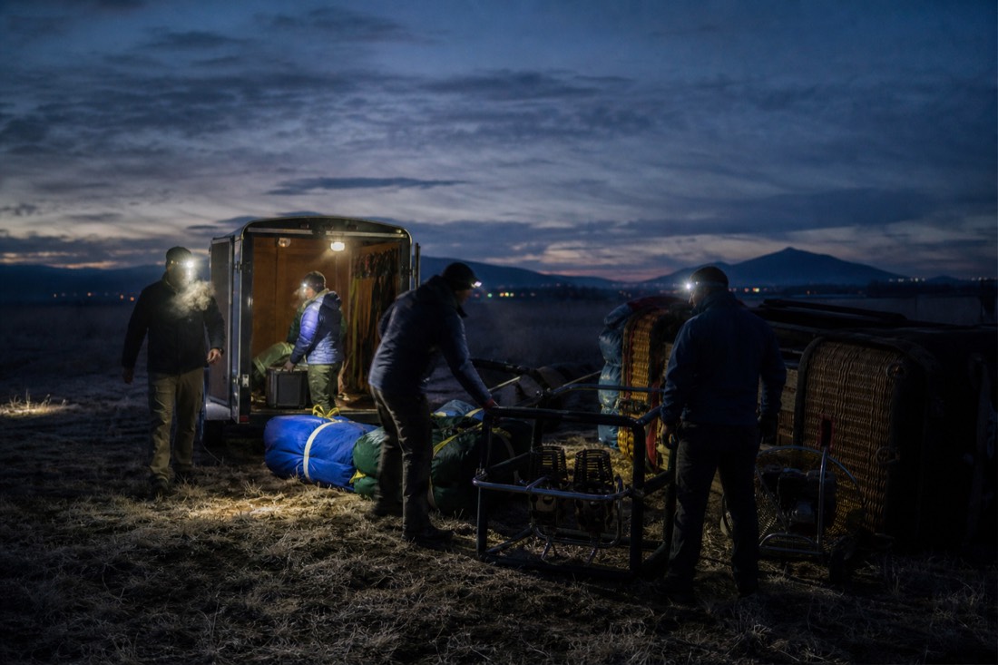 Ground crew unloading balloon equipment onto a dark field before dawn