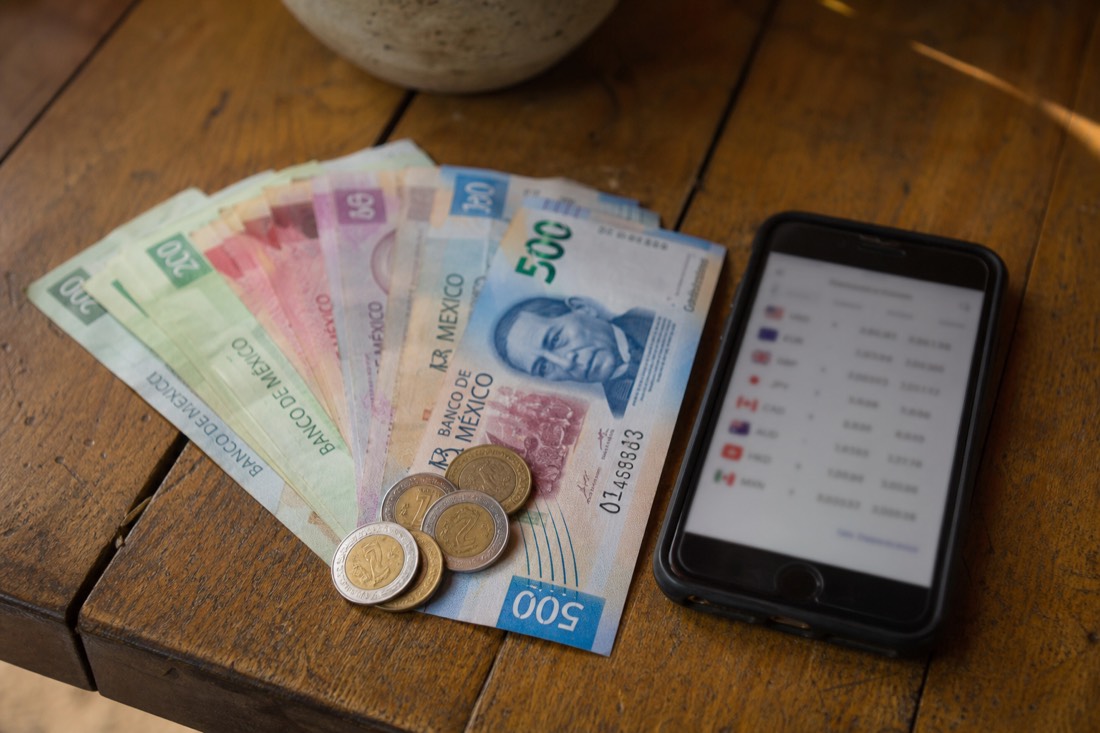 Mexican peso banknotes and coins beside a phone showing a currency conversion screen
