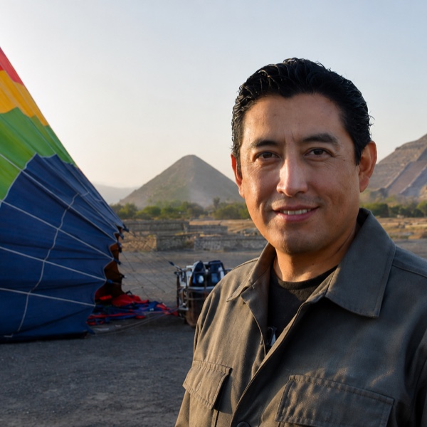 Alejandro Ramírez standing beside a hot air balloon envelope with the Pyramid of the Sun behind him at Teotihuacan